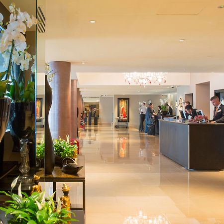 The May Fair, A Radisson Collection Hotel, Mayfair London Exterior photo The photo shows a spacious and elegantly designed hotel lobby. There are decorative elements such as flowers and plants along the sides, enhancing the luxurious atmosphere. In the background, you can see the reception area with staff members engaged 