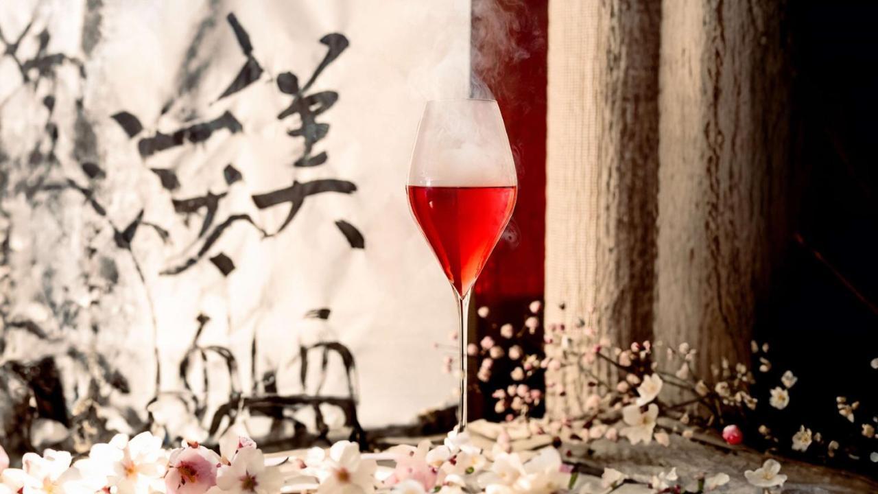 The May Fair, A Radisson Collection Hotel, Mayfair London Exterior photo The photo features a glass of red beverage, elegantly presented in a stemmed glass. The drink emits a mist, adding an ethereal quality to the image. Surrounding the glass are delicate pink flowers, enhancing the aesthetic appeal. In the background, t