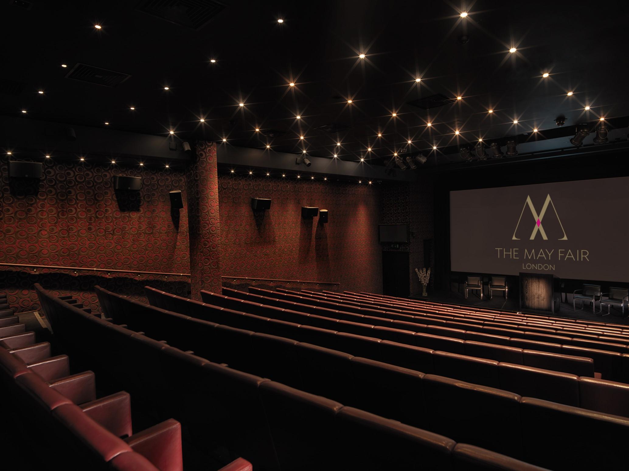 The May Fair, A Radisson Collection Hotel, Mayfair London Exterior photo The photo shows the interior of a movie theater named "The May Fair." The venue features a spacious auditorium with dark, plush seating arranged in rows facing a large screen at the front. The walls are brick, and the ceiling is adorned with numerous
