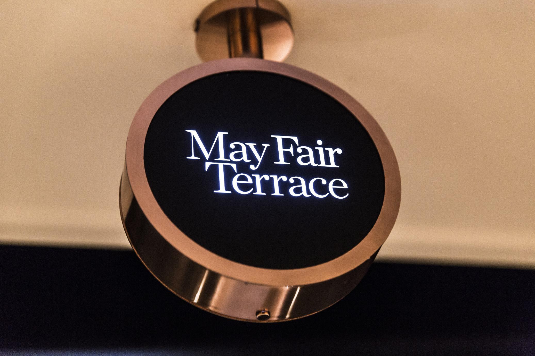 The May Fair, A Radisson Collection Hotel, Mayfair London Exterior photo The image shows a round sign with the text "May Fair Terrace" displayed in a stylish font. The sign is likely illuminated and mounted on a wall or ceiling, featuring a sleek design with a dark background and a metallic border, giving it a modern aest