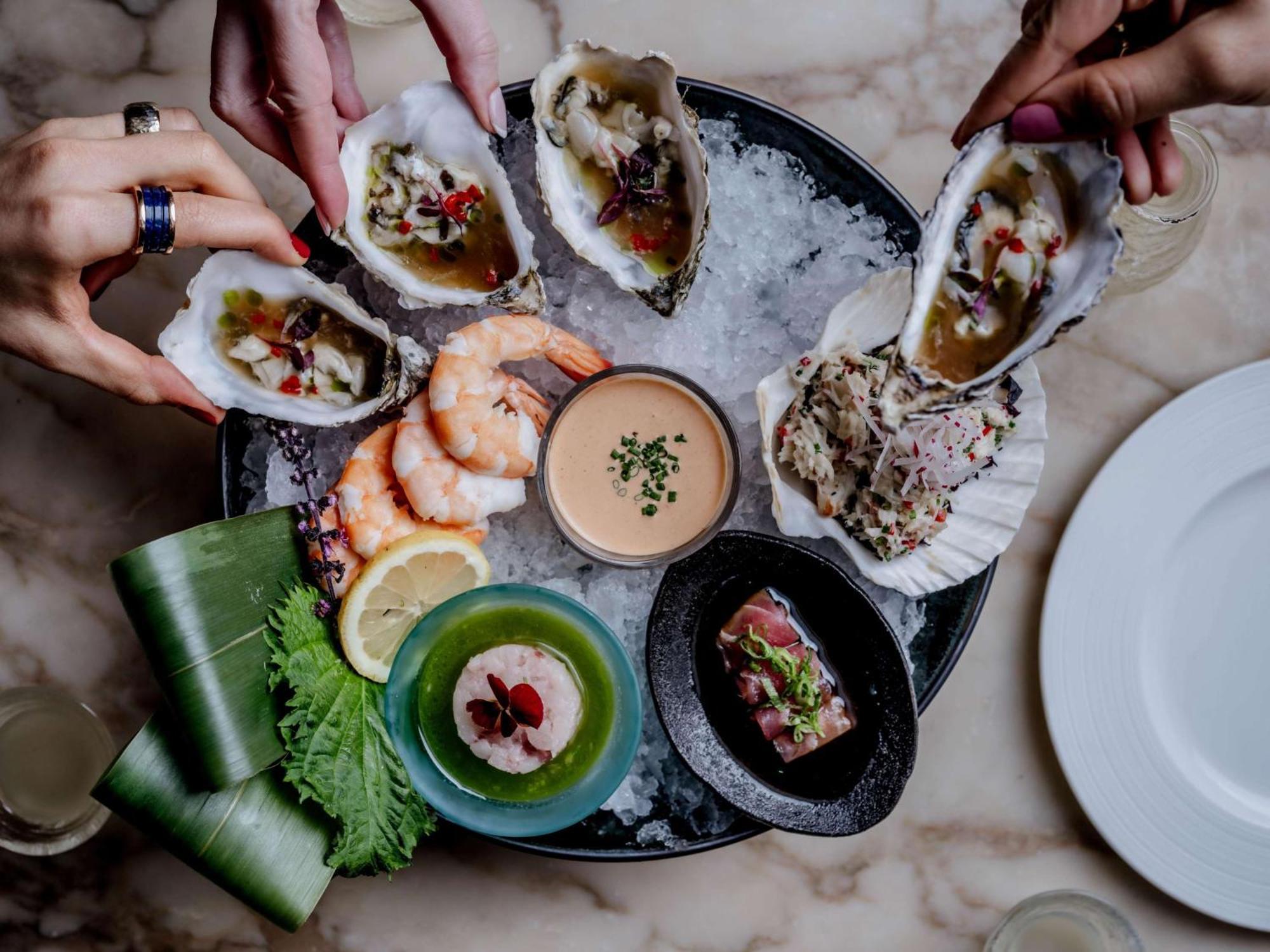 The May Fair, A Radisson Collection Hotel, Mayfair London Exterior photo The photo displays a seafood platter arranged beautifully on a round dish filled with ice. Various types of seafood are presented, including several open oysters topped with garnishes, shrimp, and a small dish of sauce in the center. Surrounding the 